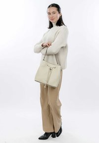 Cream leather bucket bag with drawstring closure and gold hardware accents, paired with a cream knit sweater and beige wide-leg pants.