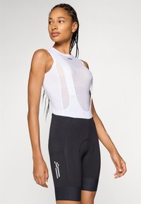 Balts velosipēdu krekls ar acs paneļiem un melni bikses ar krūšautu, kas iekļauj polsterētu sēdekli, atstarojošiem akcentiem un pieguļošu dizainu.