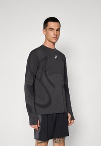 Long-sleeve athletic shirt in dark gray fabric with a textured pattern and logo. Features fitted sleeves and a crew neck design.