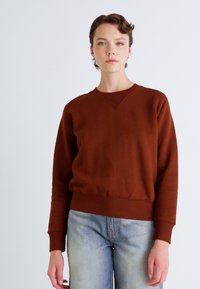 Sudadera marrón con cuello redondo, mangas largas y puños y dobladillo acanalados, combinada con jeans rectos de color azul claro. Textura suave.