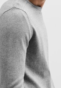 Pull gris à manches longues en tissu doux, avec un col rond et une texture lisse, présentant des coutures minimales et sans motifs apparents.