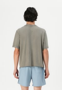 Grå bomull t-skjorte med avslappet passform, korte ermer og rå kant. Brukt med lyseblå shorts, som viser en uformell stil.