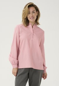 Rosa langærmet bluse med mandarin-krave, knaplukning og let puffede ærmer, lavet af et struktureret stof.