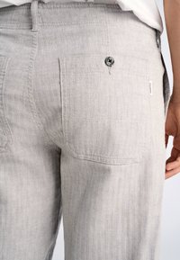 Lichtgrijze broek met een visgraatpatroon, voorzien van een achterzak en een knoopdetail. Heeft een rechte pijp en een gestikte stof.