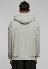 Sudadera con capucha de color gris claro, de corte relajado, con hombros caídos y puños y dobladillo de canalé. Cuenta con una gran capucha de tela suave.