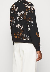 Sudadera negra con patrón floral en blanco y marrón, puños y dobladillo acanalados, corte relajado y cuello redondo.