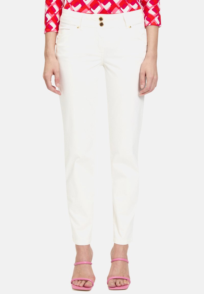 Pantalons blancs avec deux boutons dorés à la taille, coupe droite et texture lisse. Associés à des sandales à lanières roses pour un contraste.