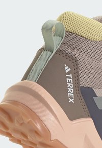 Terrex trail shoes feature a textured, brown synthetic upper, a pale pink rubber sole, and a light green heel loop for easy wear.