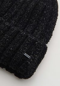 Black knitted beanie made of soft, textured yarn. Features a ribbed pattern with small beads and a black label with "Opus" on the edge.