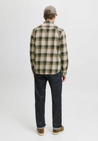 Camisa de franela a cuadros en crema, verde y negro, jeans oscuros y zapatos marrones, vista desde la parte de atrás. Incluye puños abotonados y un dobladillo curvado.