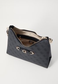 Zwarte synthetische handtas met reliëf logo-patroon, goudkleurige hardware en ritssluiting. Interieur heeft beige voering en een klein vakje.