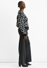 Schwarzes und weißes Leopardenmuster-Pullover, runder Ausschnitt, oversized Schnitt; kombiniert mit hochtaillierten, weit geschnittenen schwarzen Jeans und schwarzen Stiefeletten mit Absatz.