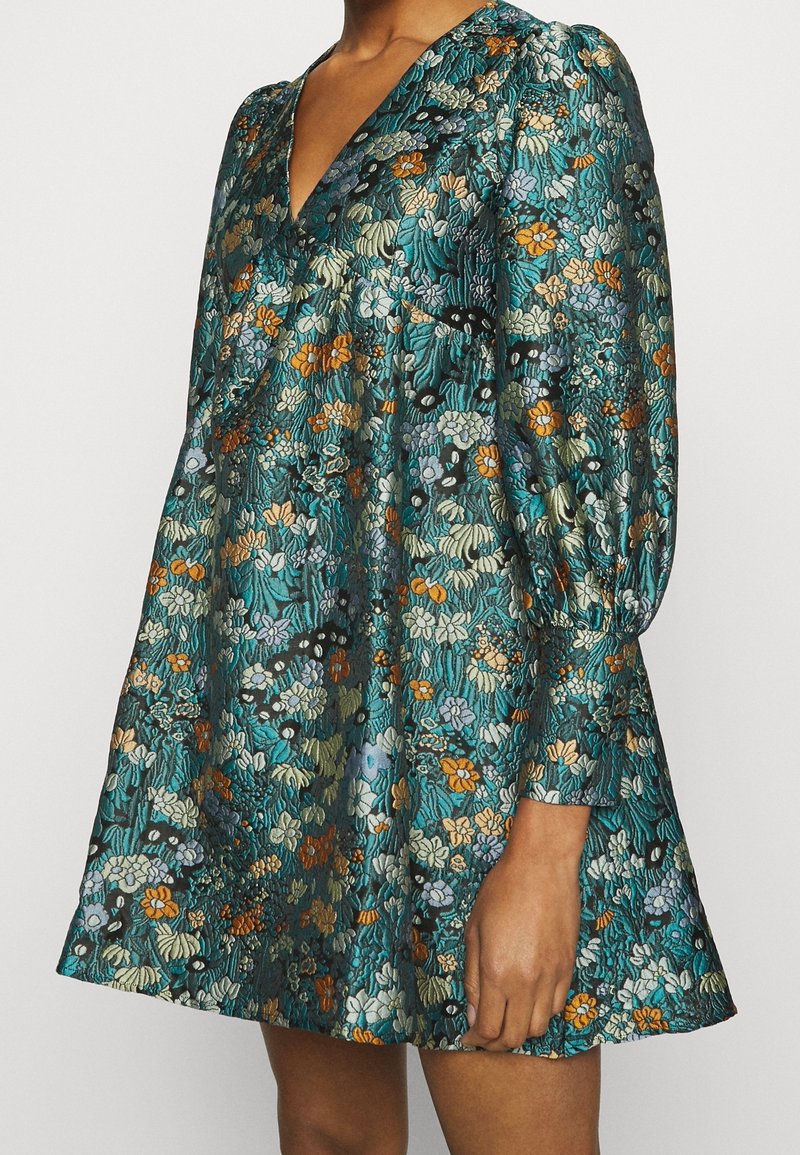 Kurzes Kleid aus türkisfarbener Stoff mit einem lebhaften Blumenmuster in den Farben Orange, Blau und Grün; V-Ausschnitt und geraffte Ärmel.