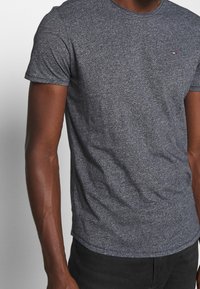 Grijze kortom mouw t-shirt van een gestructureerde stof, met een subtiele logo op de borst. Klassieke ronde halslijn met een getailleerde pasvorm.