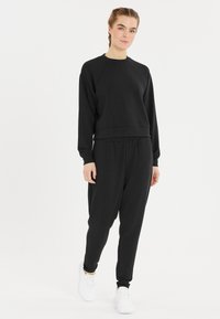 Svart sweatshirt och matchande joggers i mjukt tyg. Har rundad halsringning, ribbade muddar och avsmalnande anklar. Tillsammans med vita sneakers.