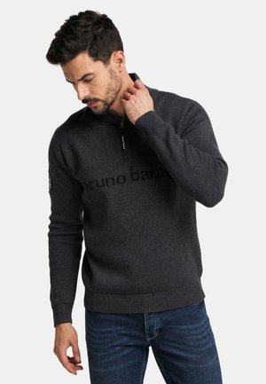 Dunkelgrauer Reißverschluss-Pullover mit hohem Kragen, der mit einem dezent gedruckten Logo versehen ist. Ribbelbündchen und -saum sorgen für Struktur. Kombiniert mit Jeans.