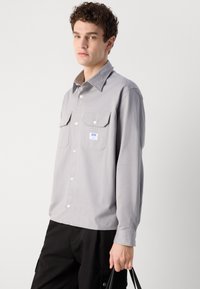 Gray button-up shirt made of lightweight fabric, featuring two chest pockets, a pointed collar, and subtle stitching details.