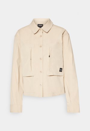 Beige cropped jack gemaakt van katoen, met een knoopsluiting aan de voorkant, twee borstzakken en lange mouwen met knoopmanchetten.