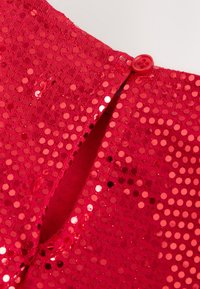 Tissu rouge recouvert de sequins brillants, avec une petite fente fermée par un bouton rouge au bord supérieur.