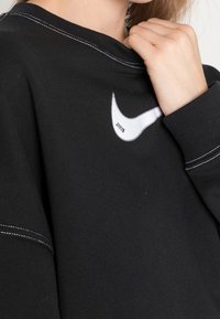 Sudadera negra con un logo de Nike blanco bordado en el frente, cuello redondo y costuras en blanco como detalle en los puños y el cuello.