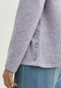 Lichtpaarse, gestructureerde trui met een zijpaneel en vier ronde, grijze knopen, gecombineerd met blauwe denim.