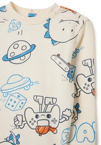 Sweatshirt crème avec des motifs de dessins animés ludiques en bleu et orange, comprenant des planètes, des manettes de jeu et diverses formes.