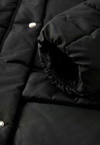 Gros plan sur une doudoune noire, affichant une manche retroussée et un bouton, mettant en avant sa texture et sa chaleur.