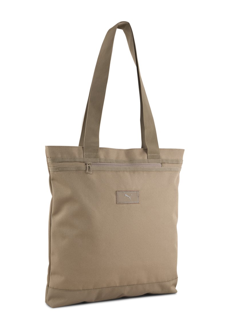 Sac fourre-tout en tissu beige, de forme rectangulaire, avec deux poignées robustes, un zip sur le dessus et une petite étiquette logo sur le devant.