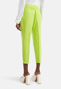 Limegröna linnebyxor med elastisk midja, knälängd och vikta muddar. Bärs med vita klackskor med blockklack.