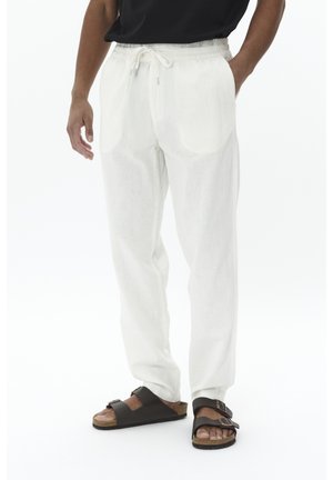 Pantaloni leggeri, bianchi, con vita elasticizzata e due tasche laterali, abbinati a sandali aperti color marrone scuro. Texture liscia, vestibilità comoda.