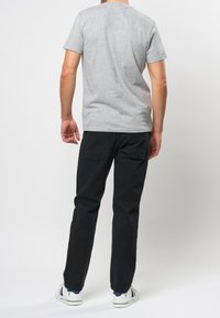 Šedé bavlněné tričko s kulatým výstřihem, kombinované s černými slim-fit kalhotami. Minimalistický design bez viditelných vzorů nebo akcentů.