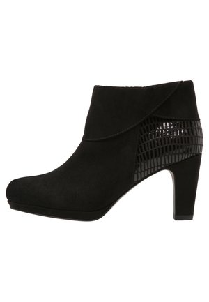 Las botas negras hasta el tobillo presentan un upper de ante con un acento de cuero charol texturizado. El diseño incluye un tacón alto y una punta redondeada.