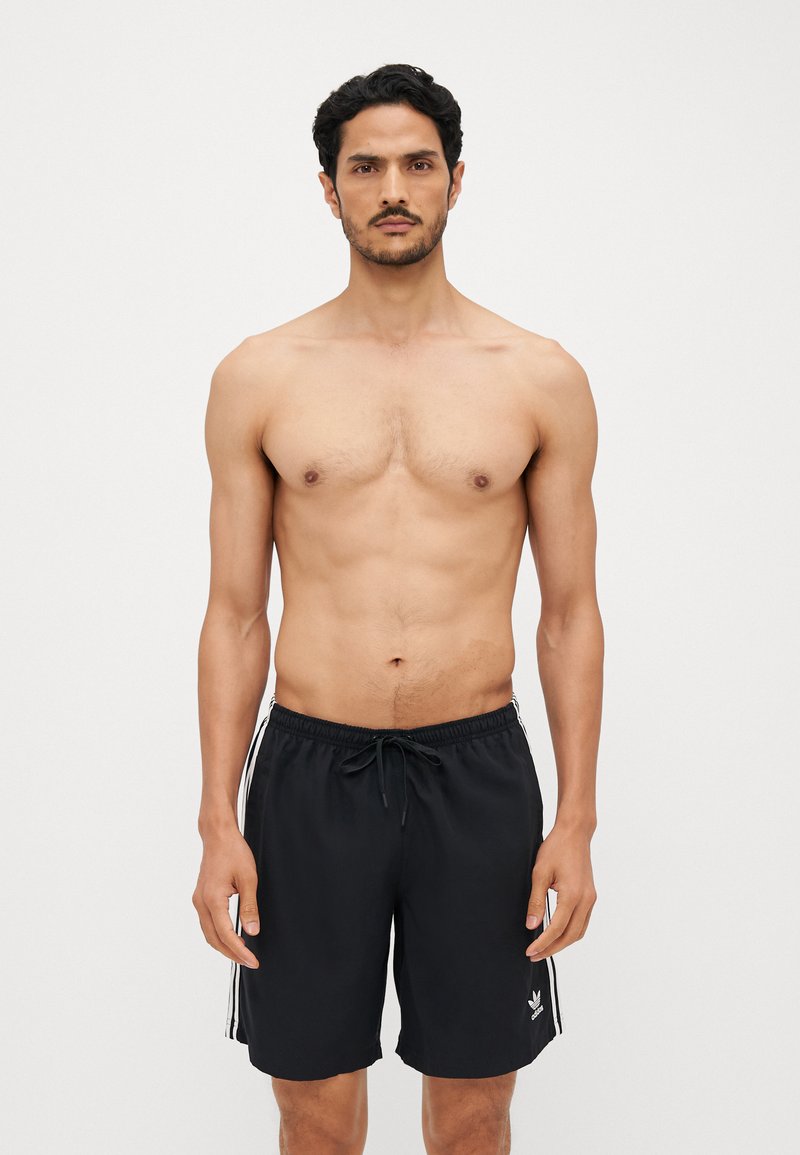 Sorte svømmeshorts med hvite sidedrakter og justerbar snor. Laget av lett materiale, med en logo på det nederste benet.