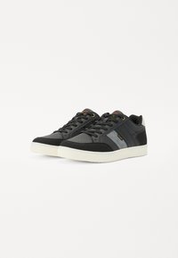 Baskets de sport noires et grises avec un design en cuir lisse et en daim, des accents texturés, des lacets plats et une semelle en caoutchouc blanche.