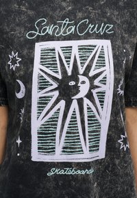 Γραφικό πρόσωπο ήλιου και φεγγαριού με ακτινωτές ακτίνες μέσα σε ορθογώνιο σε μαύρο, ξεβαμμένο μαύρο T-shirt με το κείμενο "Santa Cruz Skateboards".