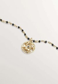 Collar de oro con un colgante circular de diseño troquelado, acentuado con una piedra negra central. Cadena de cuentas con pequeñas cuentas negras.