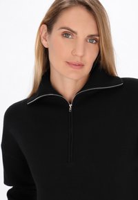 Pullover nero con colletto alto e mezza cerniera, realizzato in un morbido materiale a maglia. Presenta un design pulito e minimale senza motivi.