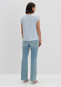 Blusa azzurro chiaro a maniche corte con uno spacco sul retro, abbinata a jeans chiari e tacchi aperti argento. Tessuto morbido e vestibilità rilassata.