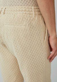 Beige gebreide broek met een ruitpatroon, voorzien van een aansluitende tailleband, zijzakken en een gestructureerd, ademend materiaal.
