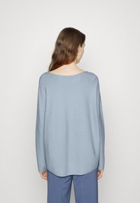 Pull ample bleu clair avec un large col rond et des manches longues. Confectionné dans un tissu doux et lisse avec un ourlet légèrement arrondi.