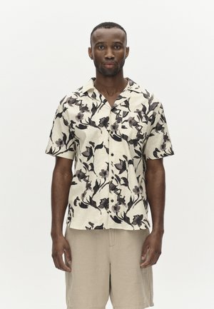 Short-sleeve shirt in light beige with black floral print. Button-down design; fabric appears textured. Paired with beige shorts.