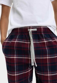 Rode en marineblauwe geruite broek met een elastische tailleband en een katoenen trekkoord. De stof heeft een soepele textuur met een geruit patroon.
