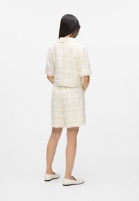 Ensemble coordonné de couleur claire et texturé comprenant un haut à manches courtes aux bords effilochés et un short assorti, tous deux à motif à carreaux.