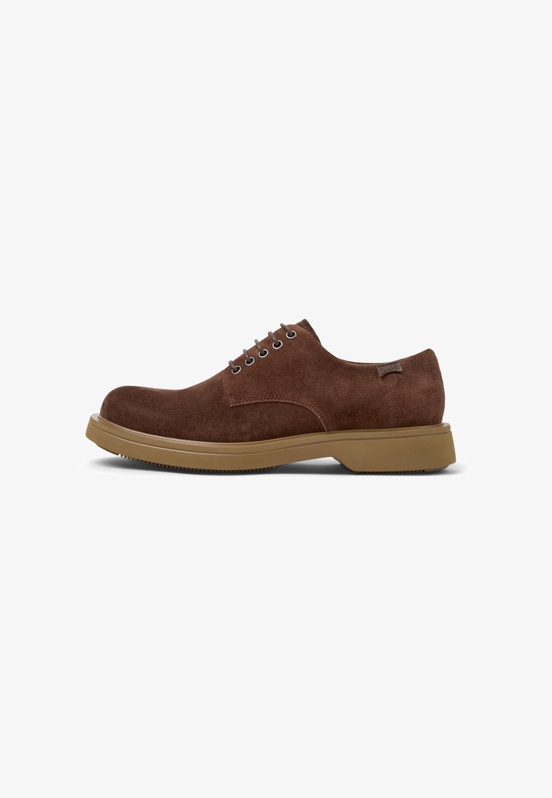 Chaussure en daim brun, à lacets, avec un bout rond et une semelle en caoutchouc robuste, placée sur un fond blanc.