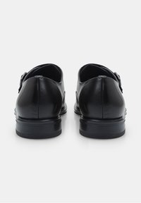 Zapatos de cuero negro con textura suave, punta redondeada y tacón bajo apilado. Presentan una hebilla decorativa en el lateral.