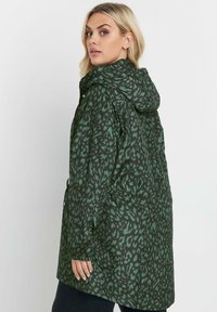 Grön leopardmönstrad regnjacka med huva, långa ärmar, elastiska manschetter och dragsko i midjan. Slätt, lättviktigt tyg och en avslappnad passform.