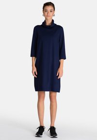 Vestido azul marino con cuello de capucha y mangas tres cuartos, confeccionado en una tela suave, que presenta un corte relajado y un dobladillo que cae por encima de las rodillas.