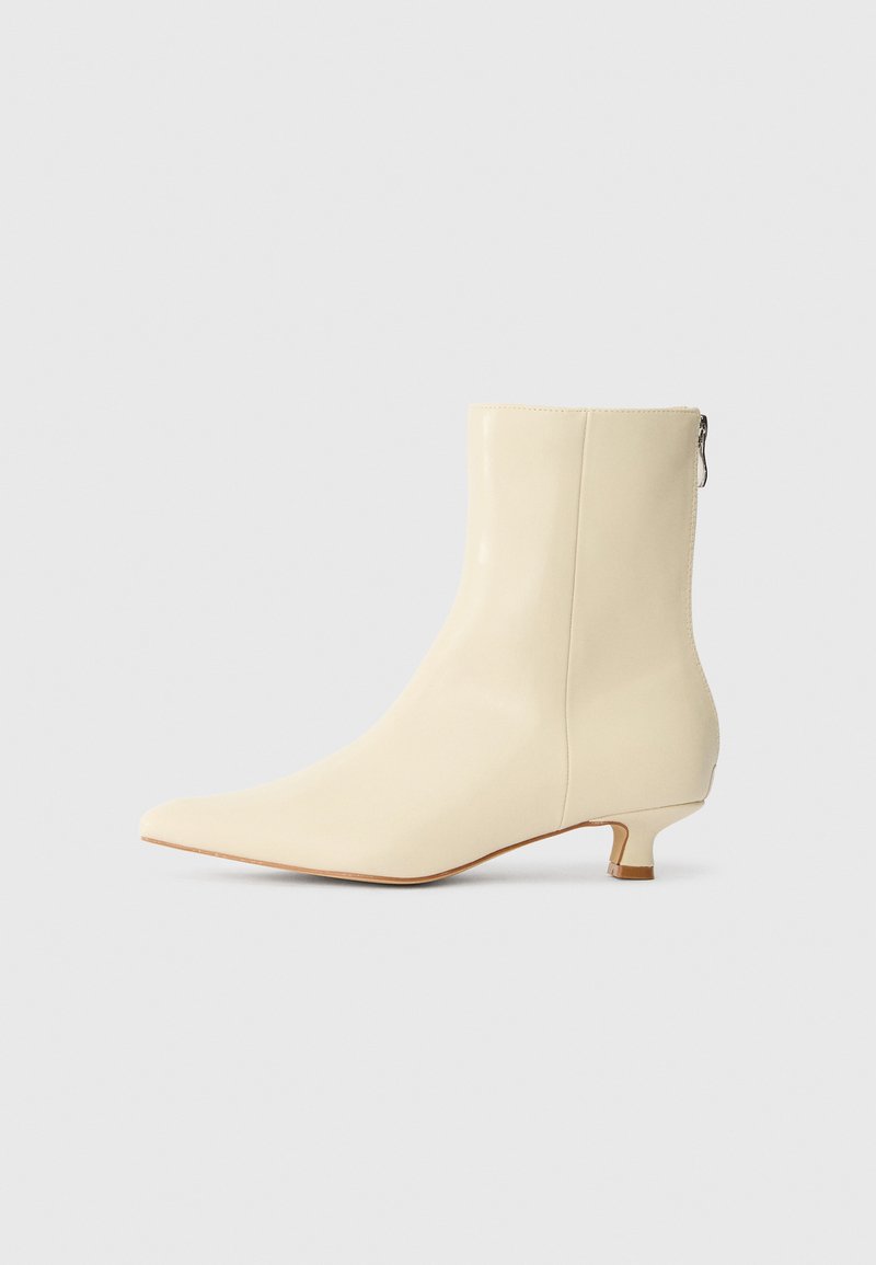 Bottine à bout pointu en cuir crème avec une finition lisse, dotée d'un petit talon bloc et d'une fermeture à glissière sur le côté.
