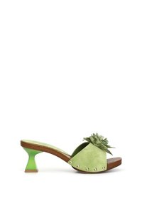 Grøn ruskinds slide-sandal med en blomsteraccent, buet træsål og en kort geometrisk hæl i solid grøn og lysebrunt.