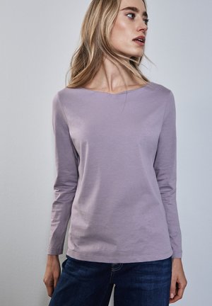 Langärmliges lavendelfarbenes Hemd mit V-Ausschnitt, aus weicher Baumwolle gefertigt, kombiniert mit dunkelblauen Jeans. Der Stoff hat eine glatte Textur.